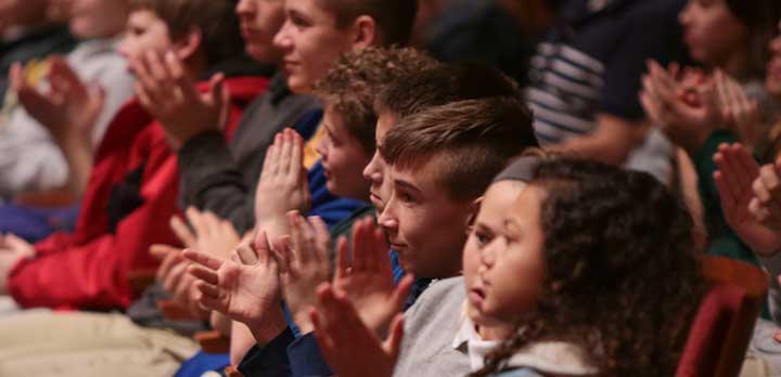 A handful of young audience members applaud during a concert