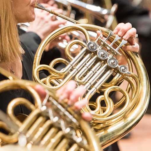 Close-up image of two people playing French horn