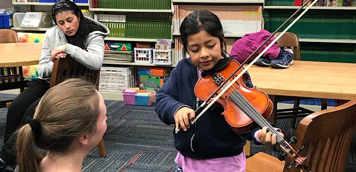 A Music Lab volunteer shows a young child how to play the violin