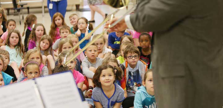 A group of grade school students watches a trombone performance